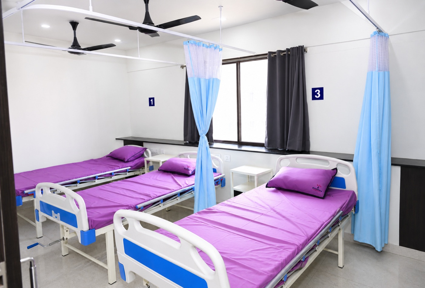 Inpatient ward with numbered beds and natural light at Sharada Hospital